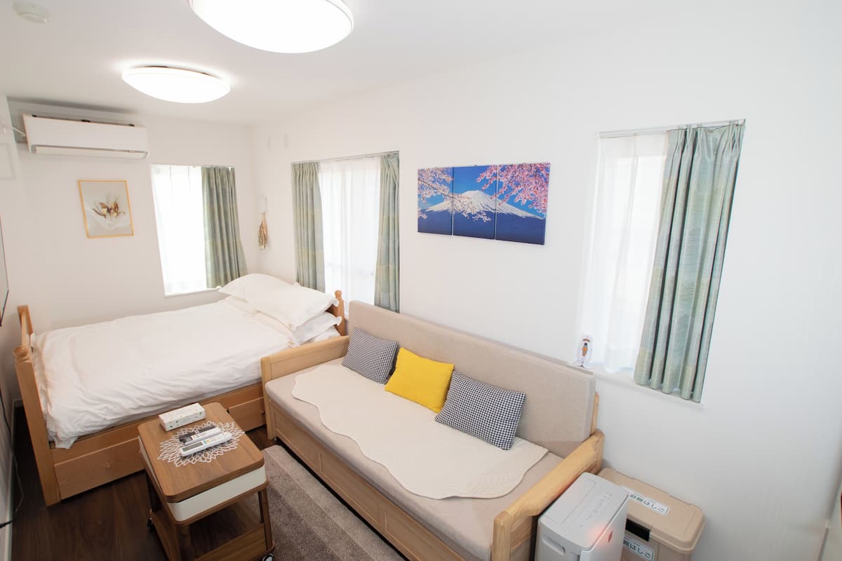 A compact room with a bed, a sofa, a small table, and a window with curtains.