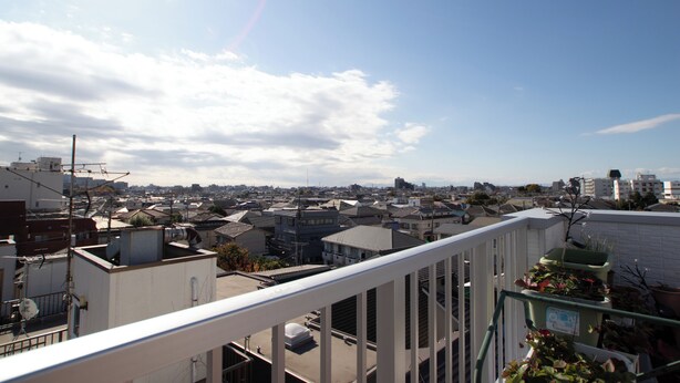 Eine Stadtansicht mit Wohnhäusern, blauem Himmel und einem Balkon mit Blumentöpfen.