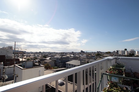 A cityscape with residential buildings, a clear sky, and a balcony with potted plants.