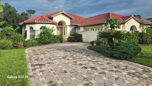 A two-story house with a red-tiled roof, a driveway with hexagonal tiles, and a well-maintained garden. - Charming 3-bedroom house with pool and WiFi in North Port in amazing community (North Port)