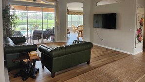 A spacious living room with a green sofa, a wooden coffee table, and a television mounted on the wall. - Charming 3-bedroom house with pool and WiFi in North Port in amazing community (North Port)