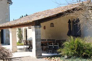 A covered outdoor seating area with chairs and tables, a tiled roof, and a building with a beige wall and a small decorative element. - EXCEPTIONAL BED & BREAKFAST IN A PROVENCAL MAS with gourmet breakfast (Châteaurenard)