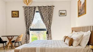 A bedroom with a bed, a desk, chairs, and a window with patterned curtains.