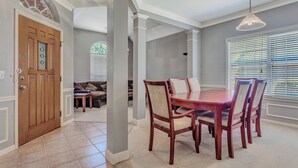 A dining area with a wooden table and chairs, a chandelier, and a view of the outdoors through large windows. - Relax in This Spacious 4BR San Antonio Home with WiFi and AC (San Antonio)