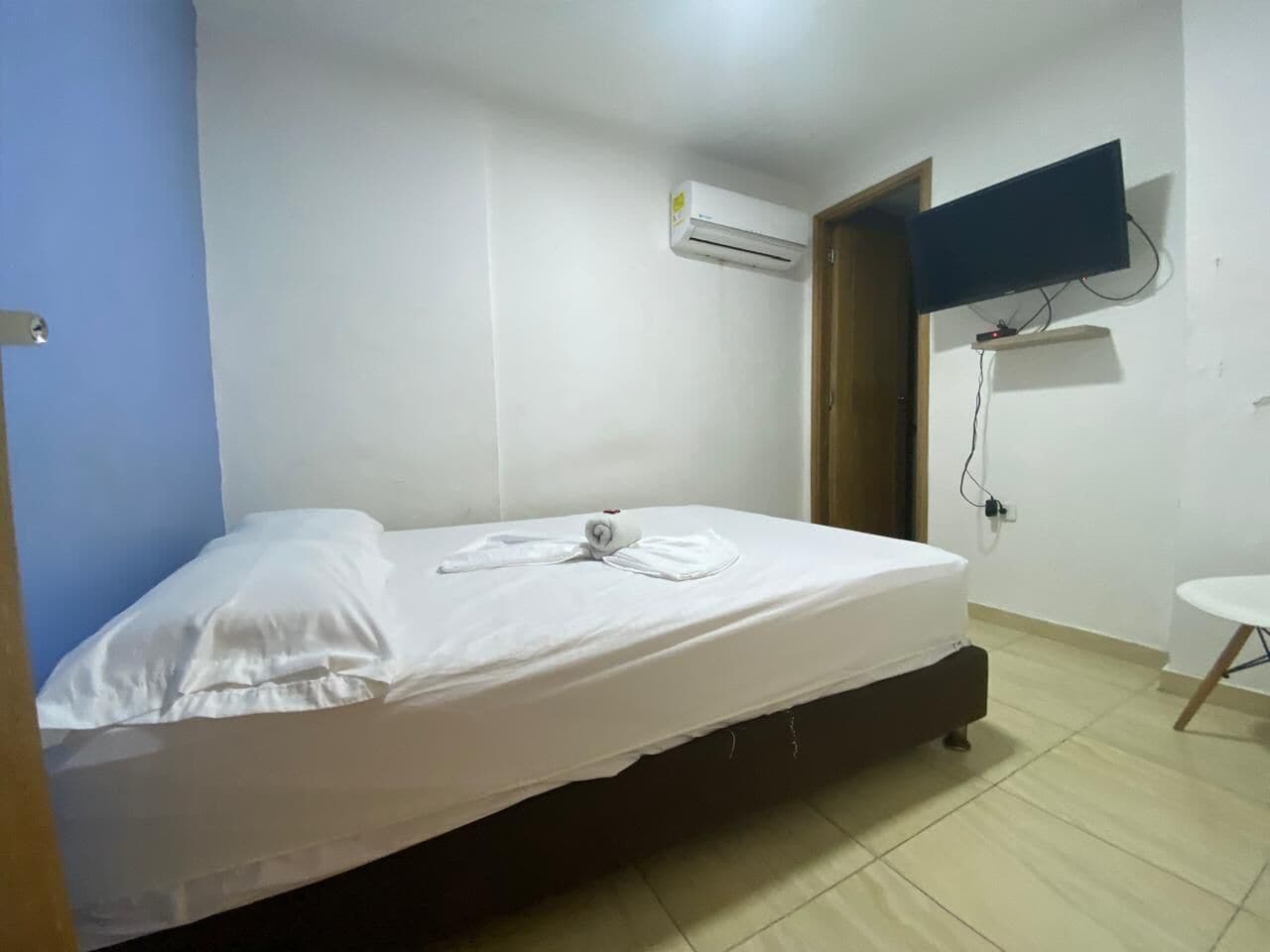 A single bed with white bedding, a mounted TV, and an air conditioning unit on the wall.