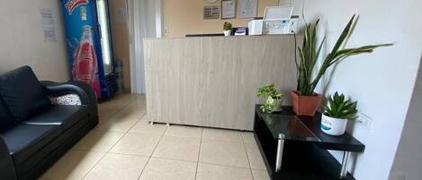 A reception area with a reception desk, a black sofa, and potted plants.
