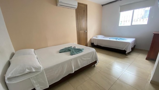 Una habitación con dos camas, una puerta, un equipo de aire acondicionado y una ventana.