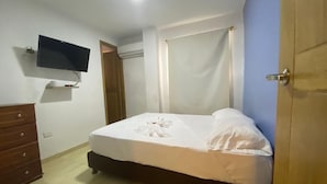 Un dormitorio con cama, cómoda, televisor montado en la pared y aire acondicionado.