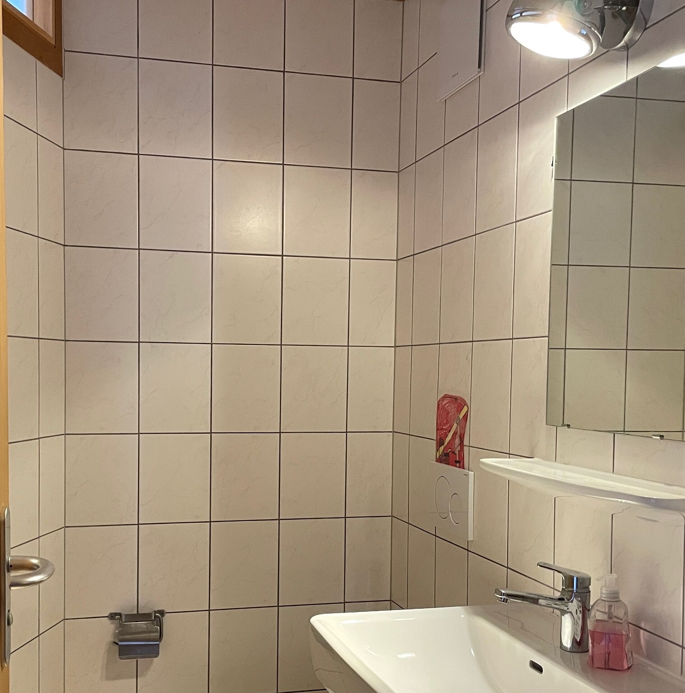 Une salle de bain avec des carreaux blancs, un lavabo, un miroir et une serviette rouge accrochée au mur.