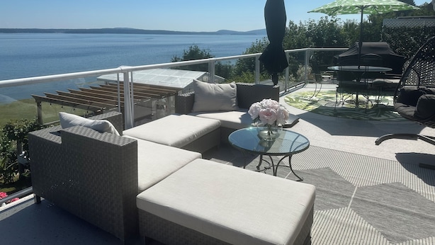 A terrace with wicker furniture, a glass table with a vase of flowers, and a view of the sea. - Oceanfront, beach access Cozy bed & breakfast loaded  amenities , Sunny Saltair (Ladysmith)