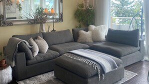 A modern living room with a grey sectional sofa, a white fluffy throw, and a chandelier. - Oceanfront, beach access Cozy bed & breakfast loaded  amenities , Sunny Saltair (Ladysmith)