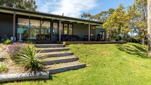 Une maison moderne dotée d’une grande façade vitrée, d’un espace extérieur aménagé et d’un jardin bien entretenu, avec des marches menant à l’entrée.
