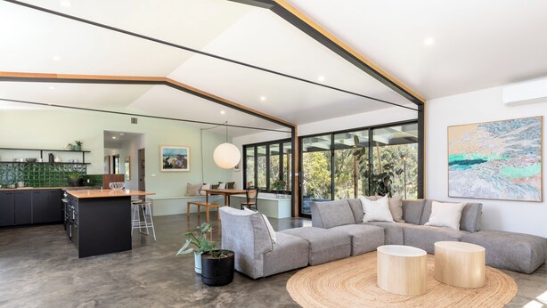 A modern living space with a kitchen, dining area, and a large sofa with a woven rug.