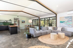 A modern living space with a kitchen, dining area, and a large sofa with a woven rug. - Tiny Lemon Farm, just 5 minutes from Bermagui! (Bermagui)