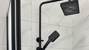 Een moderne douche met een handdouche en een vastgeschroefde douchekop, bevestigd aan een witte betegelde muur met een marmerlook.