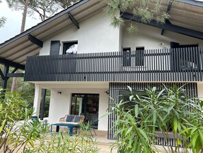 Een modern huis met twee verdiepingen, een balkon, een terras en potplanten.