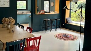 Un espace de repas moderne avec une table et des chaises en bois, un grand miroir et une vue sur l’extérieur par une fenêtre.