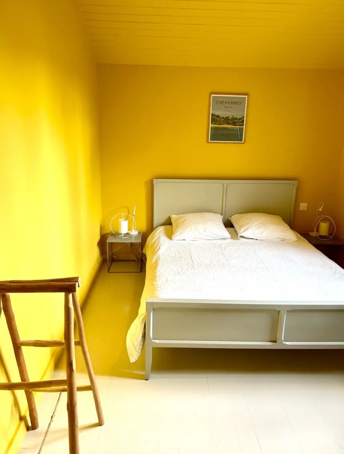 Ein Einzelbett mit Kopfteil, ein Nachttisch mit Lampe und ein kleiner Hocker.