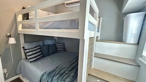 Dormitorio con literas, una escalera, una lámpara de noche y un equipo de aire acondicionado blanco.