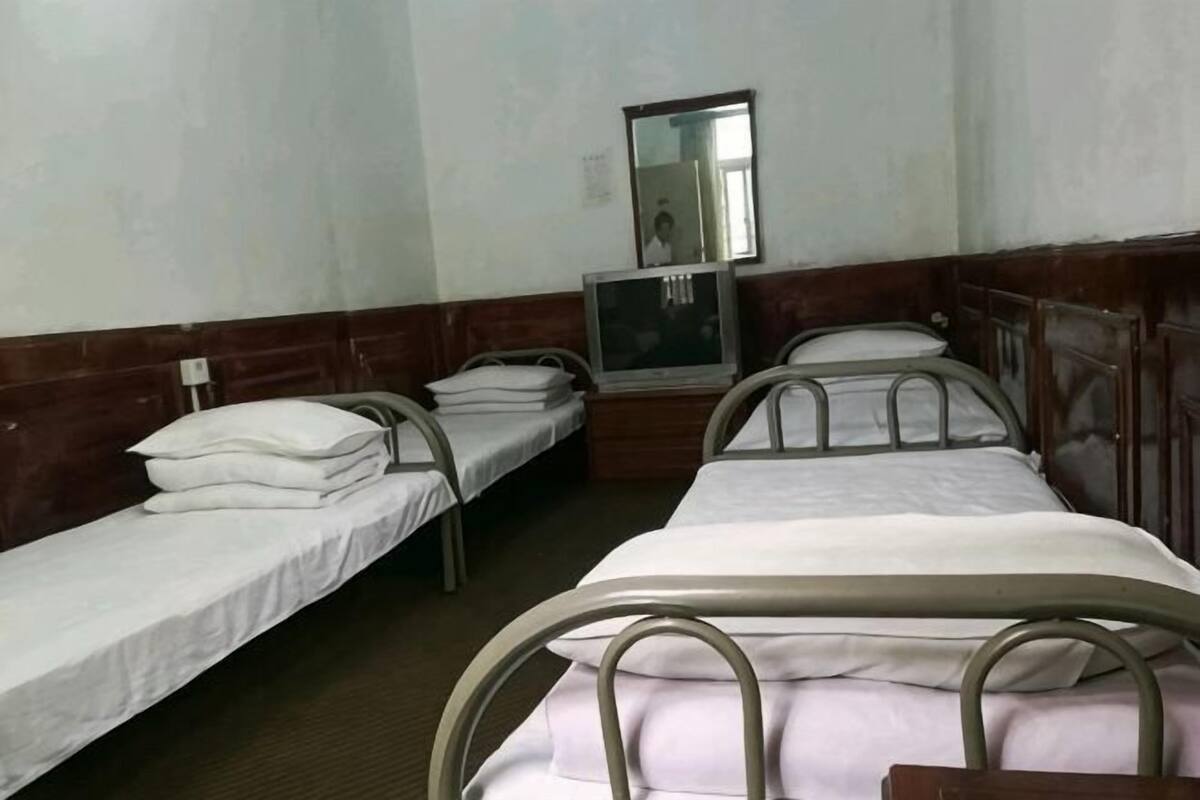 Quarto com quatro camas de solteiro, televisão e espelho na parede.