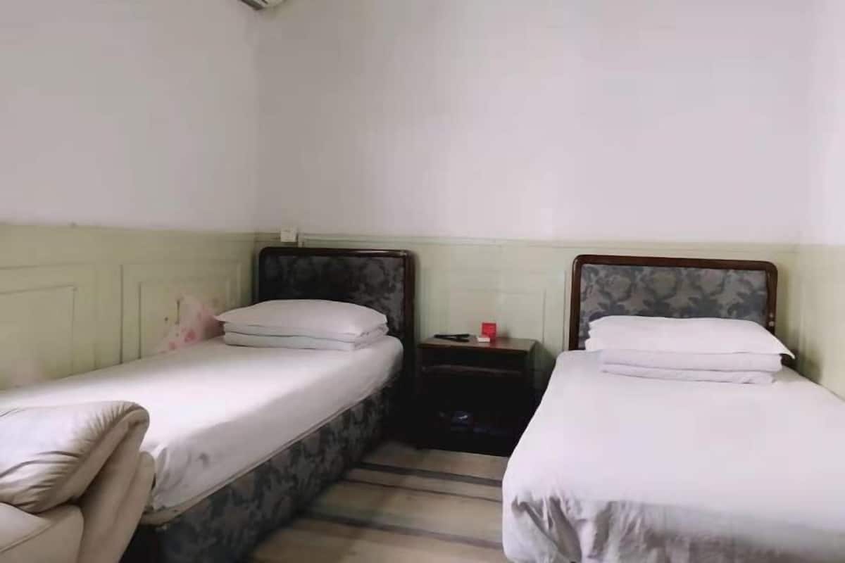 Quarto com duas camas de solteiro, uma pequena mesa de cabeceira com abajur e uma cadeira.