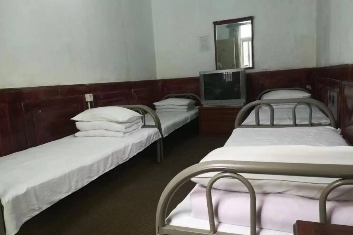 Quarto com duas camas de solteiro, televisão e espelho na parede.