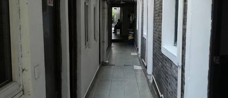 A corridor with doors on one side and windows on the other, leading to a room in the distance.