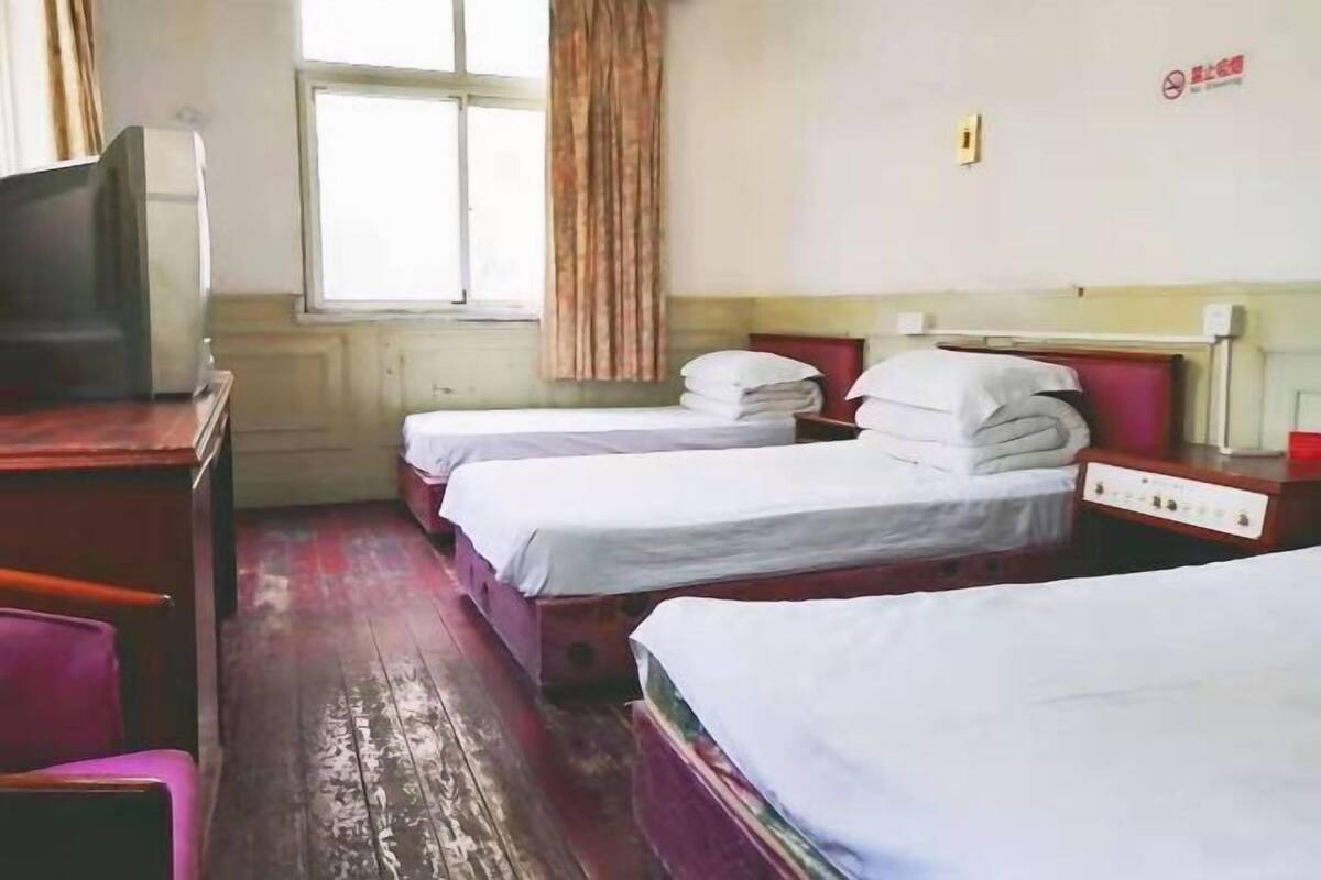 Quarto de hotel com duas camas, uma mesa de trabalho com televisão e uma janela com cortinas.