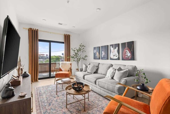 Un salon moderne avec un canapé gris, un fauteuil orange et un téléviseur à écran plat.