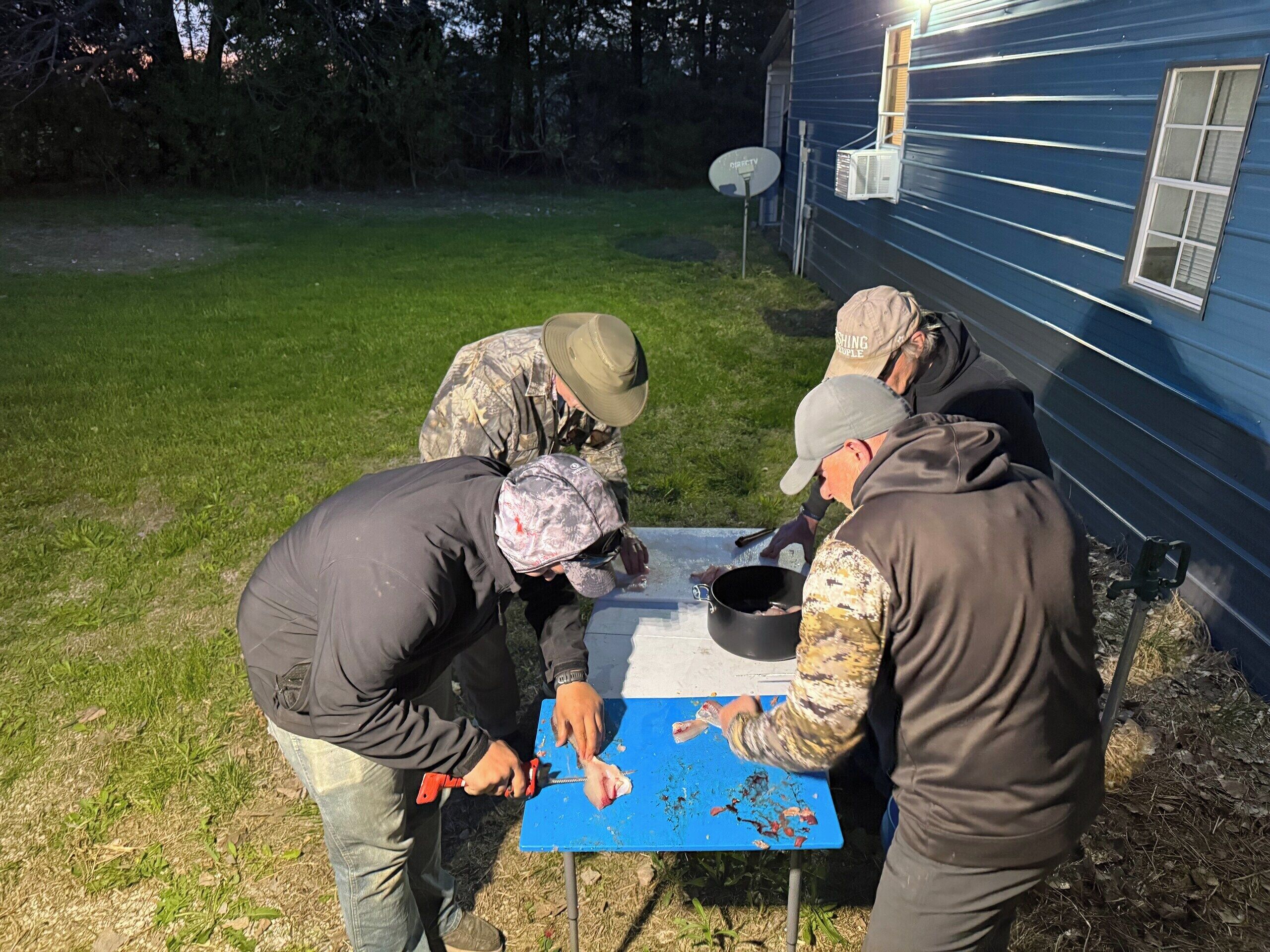 A group of people preparing food outdoors near a house with a satellite dish.