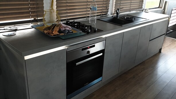 Een moderne keuken met een inbouwoven, een spoelbak en een raam met zonwering.