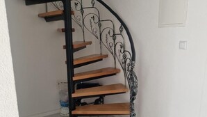 Un escalier en colimaçon avec des marches en bois et des rampes en métal noir, menant à l’étage supérieur.