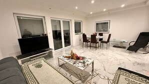 Un salon moderne doté d’un téléviseur à écran plat, d’un coin repas avec une table en verre et d’un fauteuil noir.
