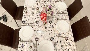 Une table à manger dressée pour six personnes, recouverte d’une nappe à motifs floraux, entourée de six chaises de couleur marron foncé.