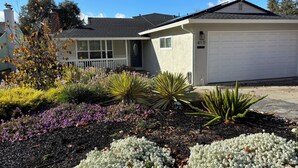 Een woonhuis met een garage, een veranda en een goed onderhouden tuin met diverse planten en bloemen.