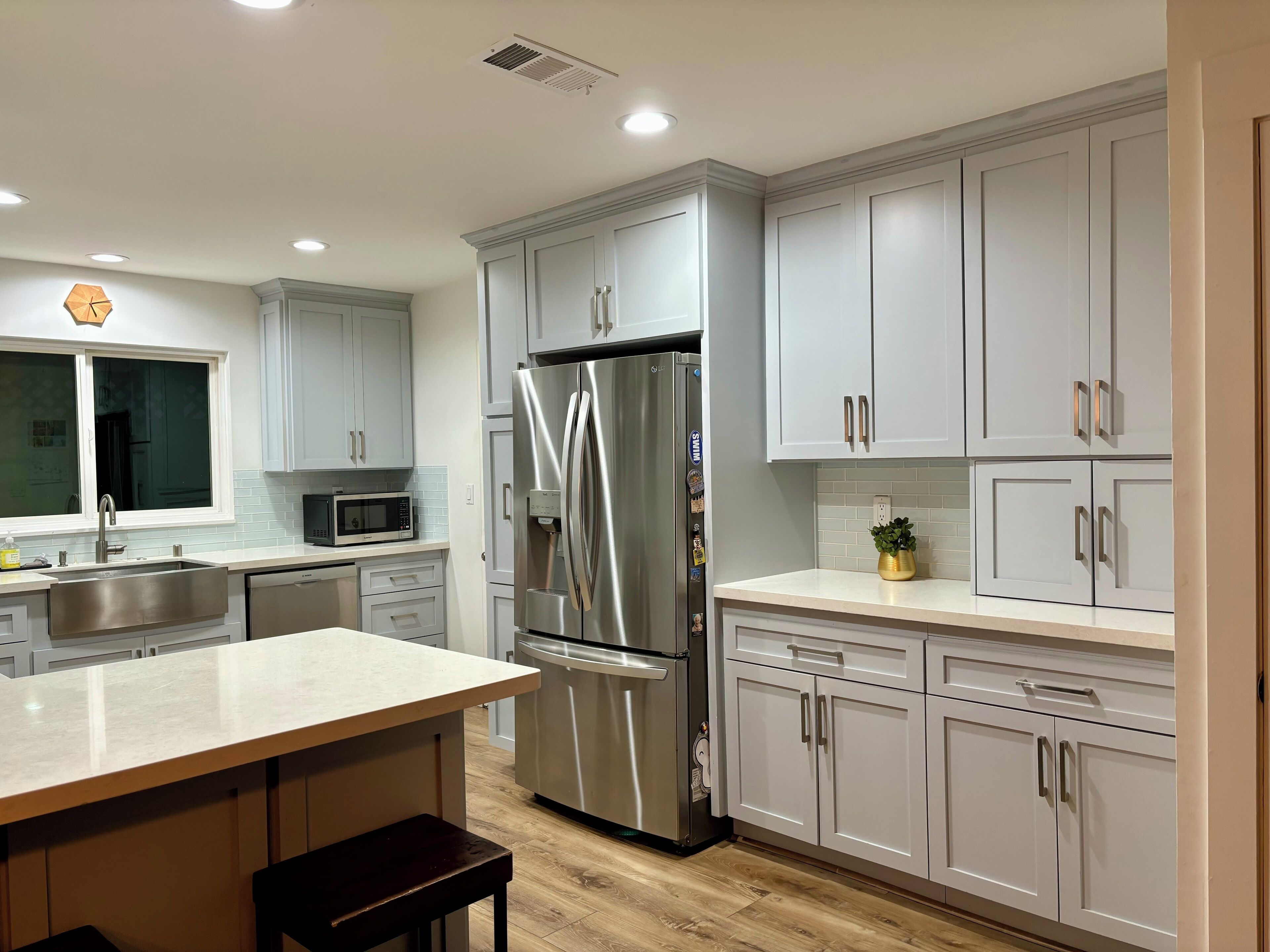 A modern kitchen with grey cabinets, stainless steel appliances, and a wooden floor.