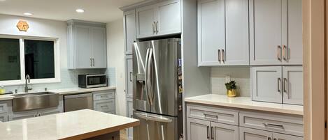 A modern kitchen with grey cabinets, stainless steel appliances, and a wooden floor.