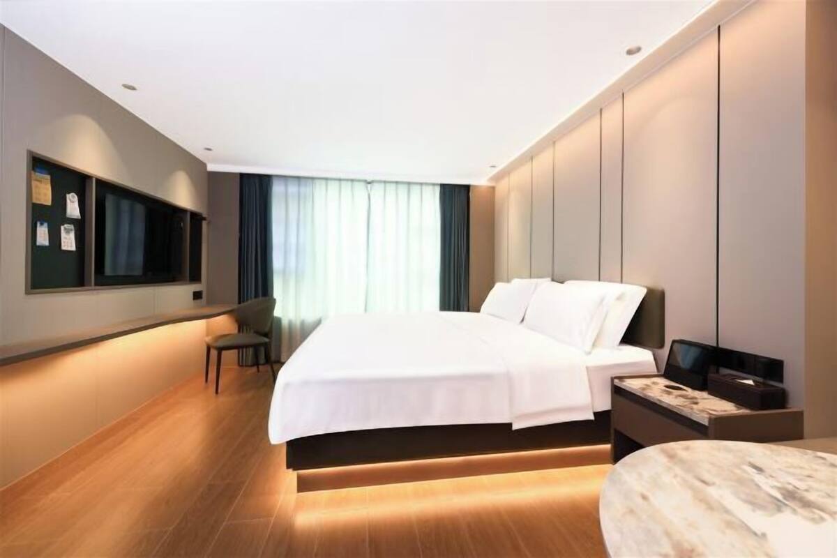 Una habitación de hotel moderna con una cama grande, un escritorio, una silla, un televisor y un estante en la pared.