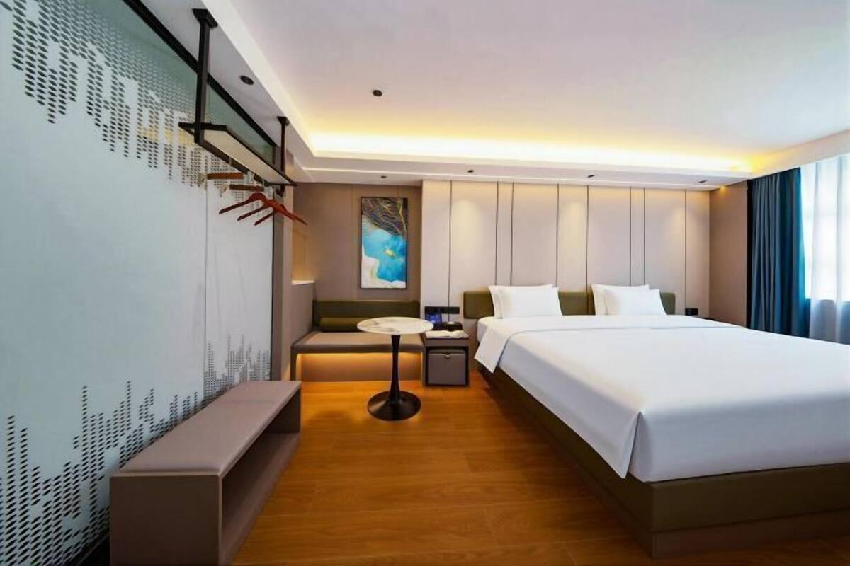Una habitación de hotel moderna con una cama grande, mesitas de noche, un escritorio y un área de descanso.