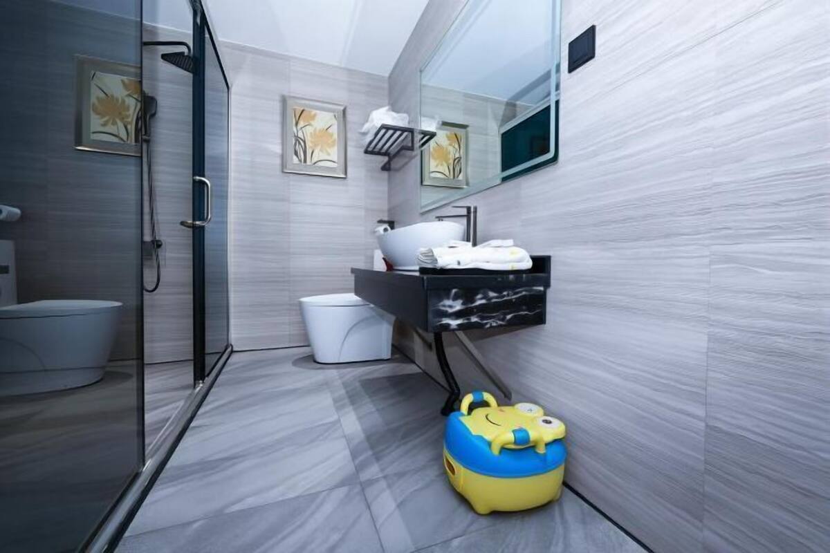 Un baño moderno con cabina de ducha de vidrio, inodoro, lavamanos con encimera negra y espejo sobre el lavamanos.