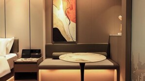 Ein modernes Hotelzimmer mit einem Bett, einem Nachttisch mit Lampe, einer Couch und einem runden Tisch mit Marmorplatte.