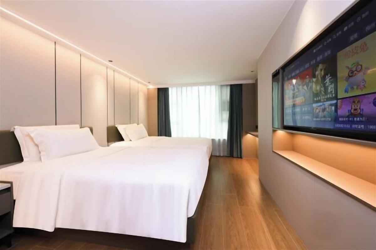 A hotel room with a large bed, a flat-screen TV mounted on the wall, and a window with curtains.