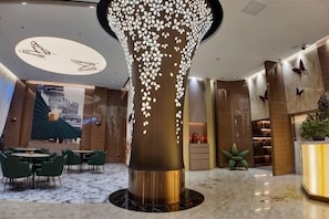 Un vestíbulo moderno con una columna decorativa central, zona de estar y mostrador de recepción.