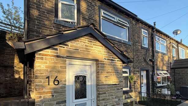 Une maison à deux étages, construite en briques, avec une porte d’entrée blanche, le numéro 16, et un petit porche.