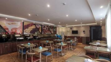 Un restaurante con varias mesas y sillas, una barra con una máquina de café y una pared con una exhibición de frutas y postres.