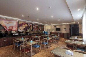 Ein Restaurant mit mehreren Tischen und Stühlen, einer Theke mit einer Kaffeemaschine und einer Wand mit einer Präsentation von Obst und Desserts.