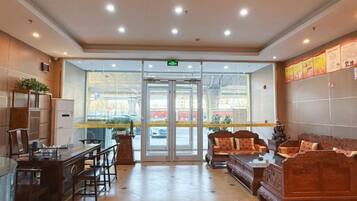 Un vestíbulo de hotel con mostrador de recepción, zona de estar y puerta de cristal de entrada.