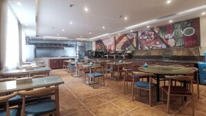 Un restaurant doté de nombreuses tables et chaises, d’un espace cuisine et d’une fresque murale illustrant des aliments.
