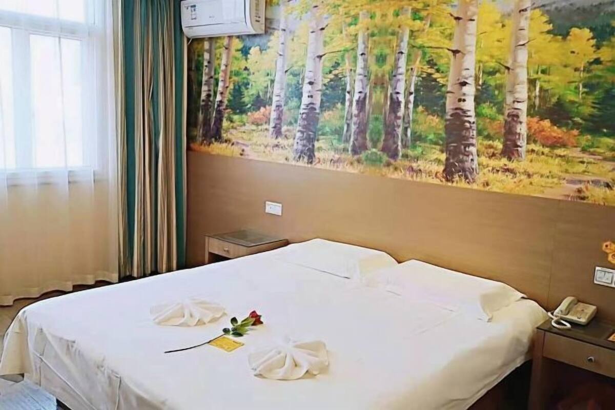 Une chambre d’hôtel avec un grand tableau représentant des bouleaux, un lit soigneusement fait avec des serviettes, un téléphone sur la table de chevet et une fenêtre avec des rideaux.