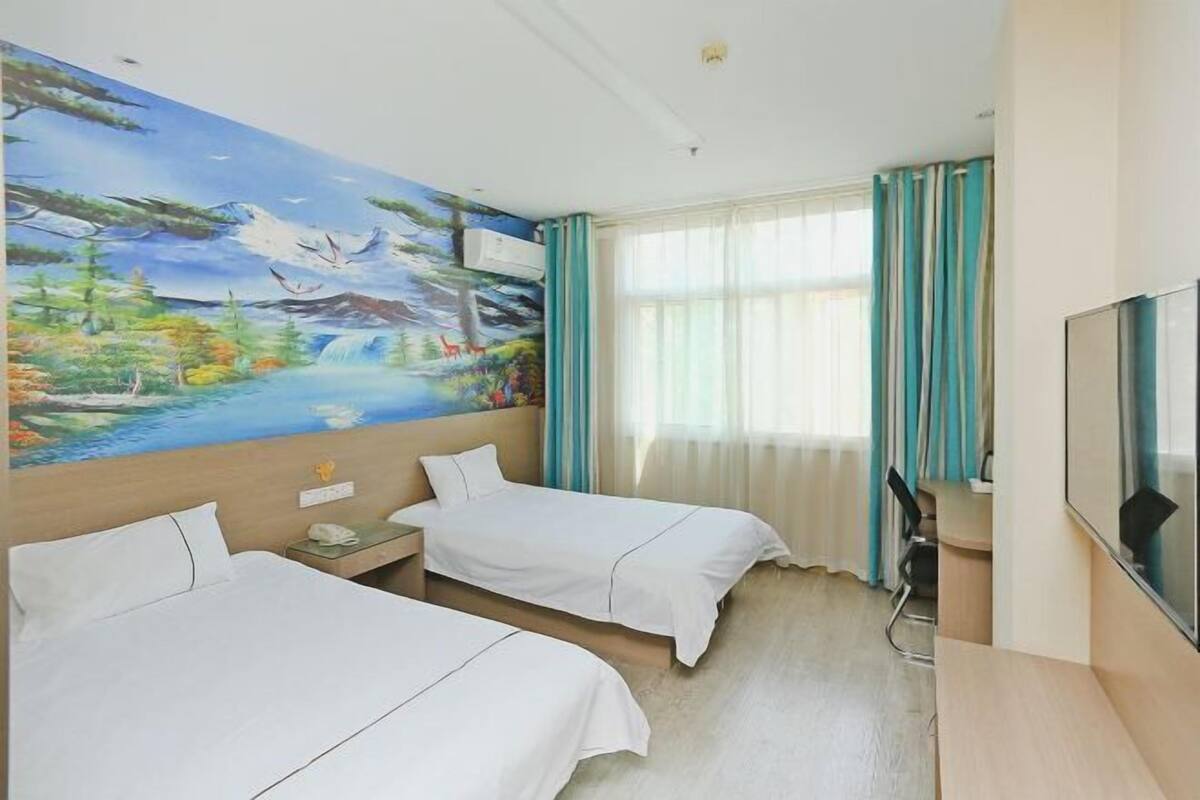 Une chambre d’hôtel avec deux lits, une grande fresque représentant un paysage, un bureau avec une chaise et un téléviseur fixé au mur.